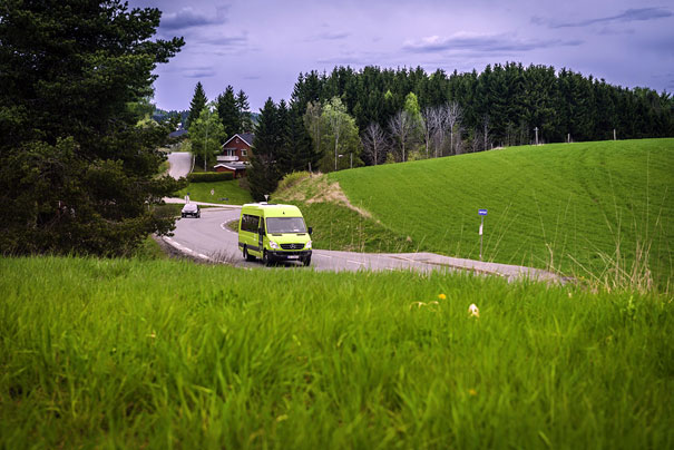 Grønn minibuss i grønt kulturlandskap. Foto.