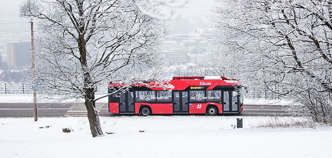 Rød bybuss i vinterlandskap sett fra siden.